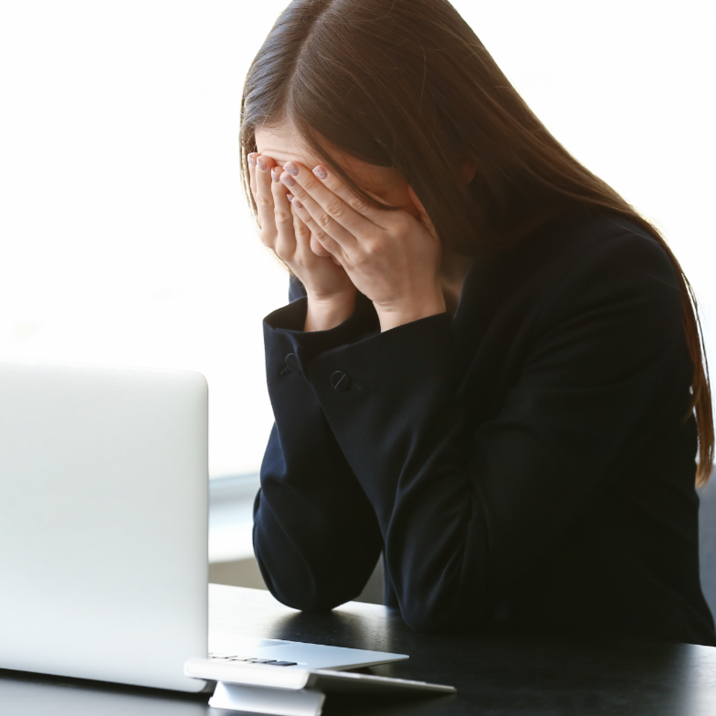woman crying at computer with hands over face.